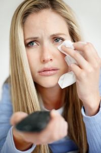 Closeup of a young blond woman with remote control watching TV and crying