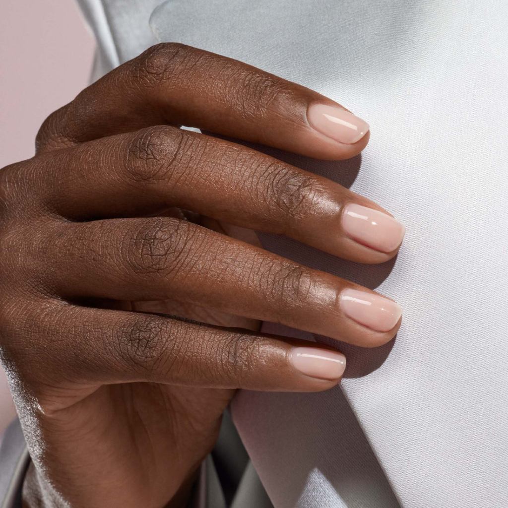 Close-up of a hand with polished nude nails resting on a light fabric surface.