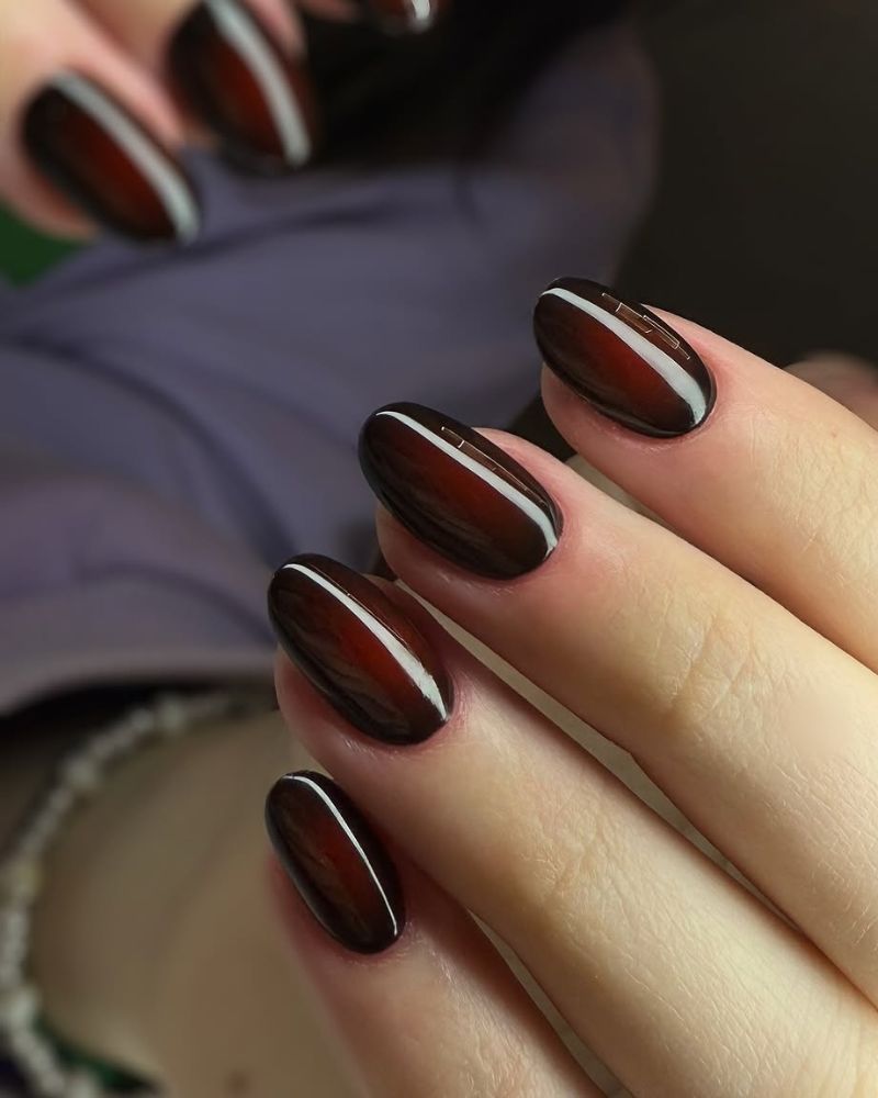 Close-up of hands showing manicured nails with a glossy dark burgundy nail polish.