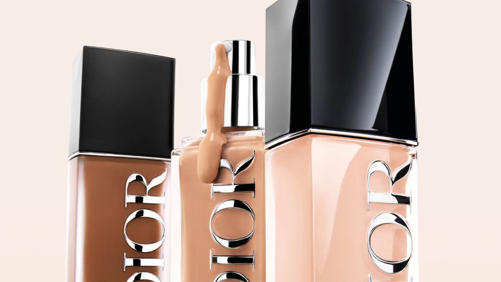 Three bottles of Dior foundation in varying shades with one bottle having a drop of foundation on the side, set against a soft neutral background.