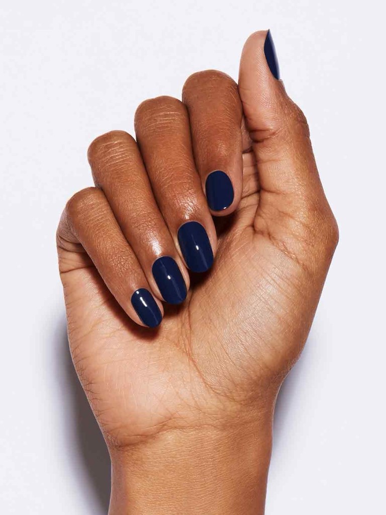 A hand displaying manicured nails painted in a dark navy blue color against a light background.