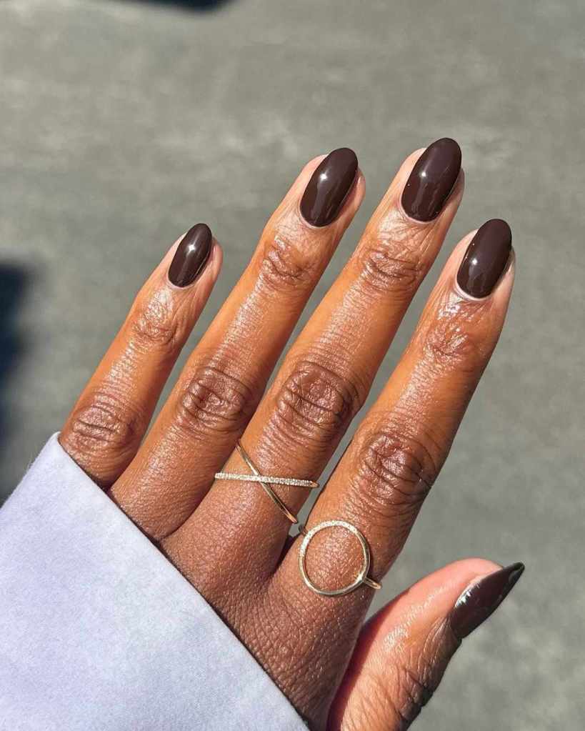 A hand with brown polished nails adorned with two gold rings, one with a diamond accent and the other in a circular design.