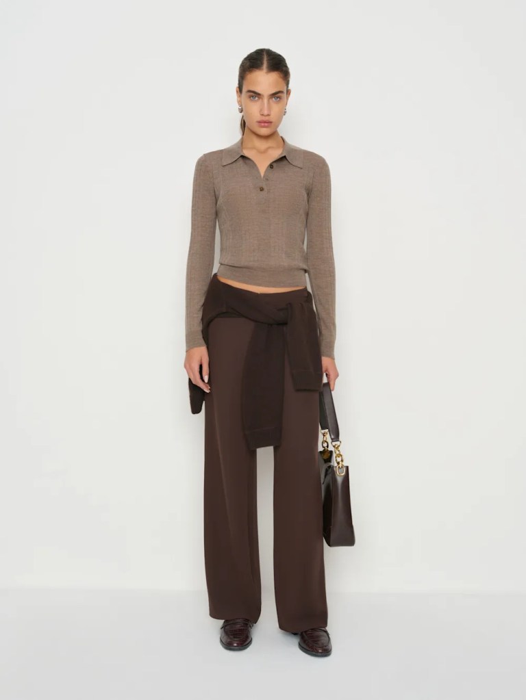 A model wearing a fitted brown long-sleeve polo top and wide-leg brown trousers, holding a dark handbag.