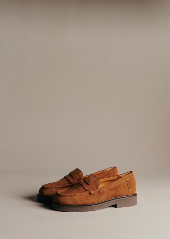 A pair of brown suede loafers displayed on a neutral background.