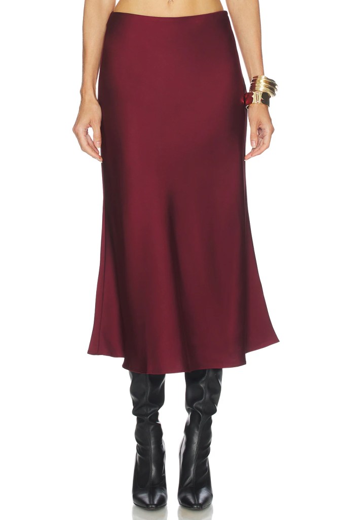 A model wearing a burgundy satin midi skirt paired with black high-heeled boots.