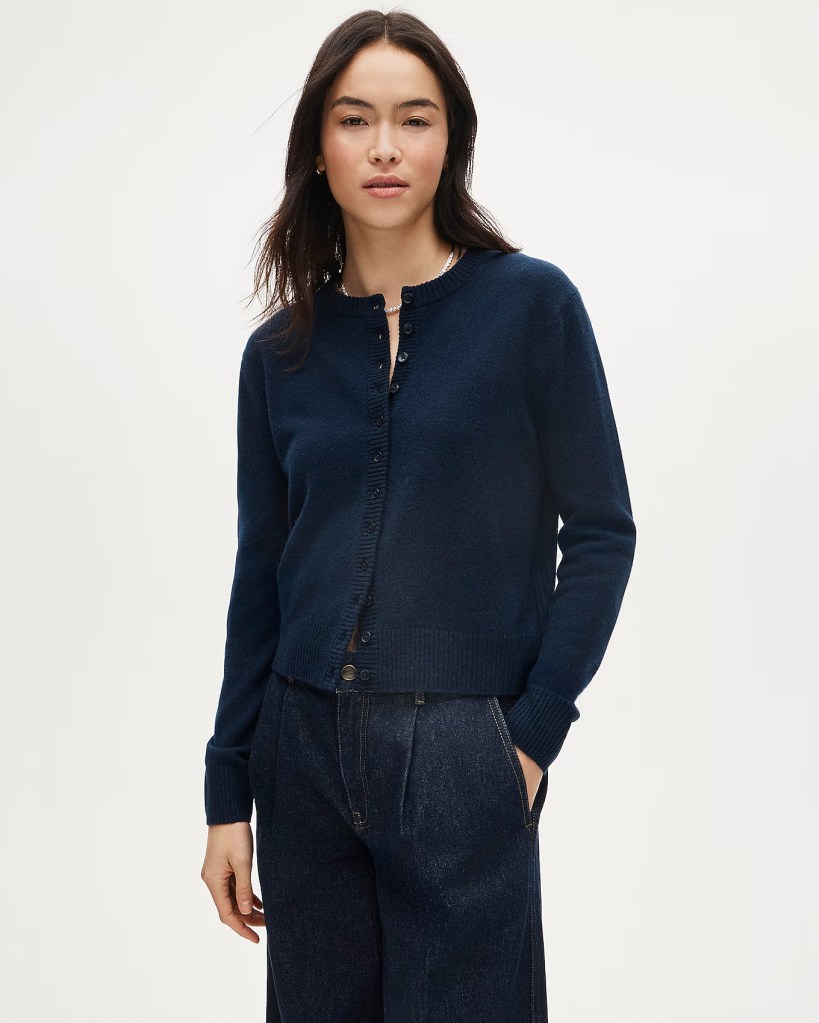 A woman wearing a navy blue cardigan, standing with her hands in her pockets, paired with dark denim pants.