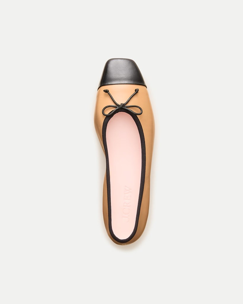 Top view of a ballet flat shoe featuring a black cap toe and a tan body, with a decorative bow detail on the front.