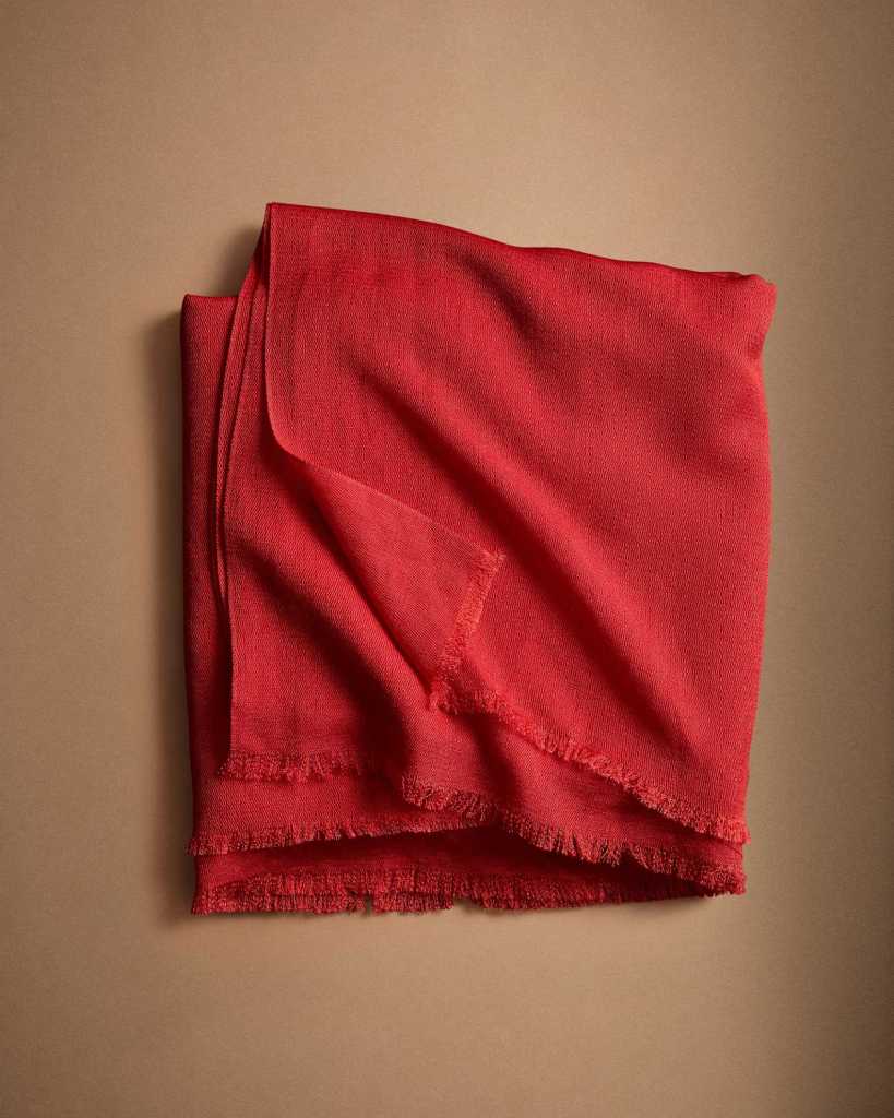 A folded red scarf with fringed edges, set against a brown background.