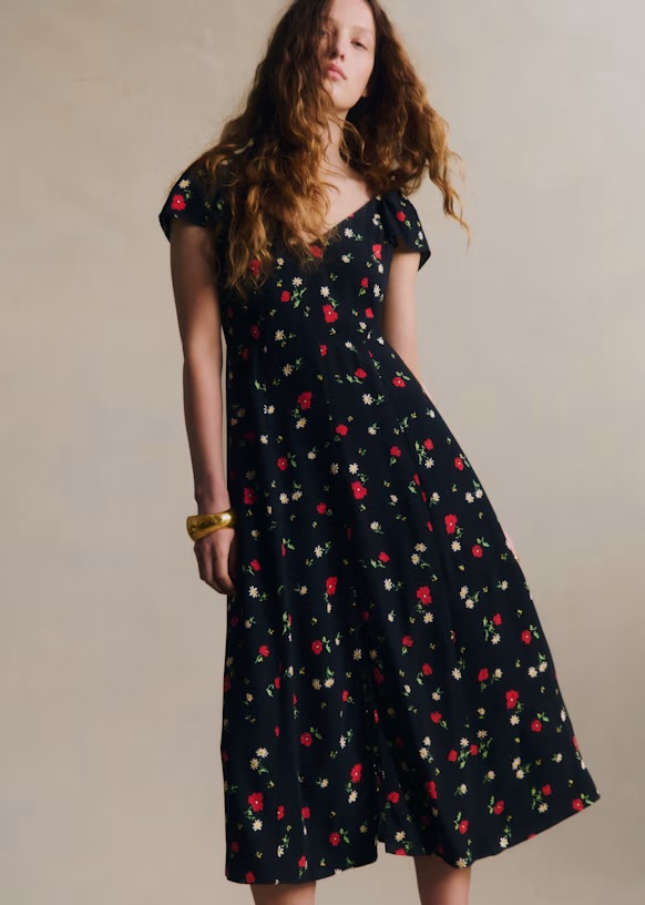 A model wearing a black floral dress with red and white patterns, posing against a neutral background.