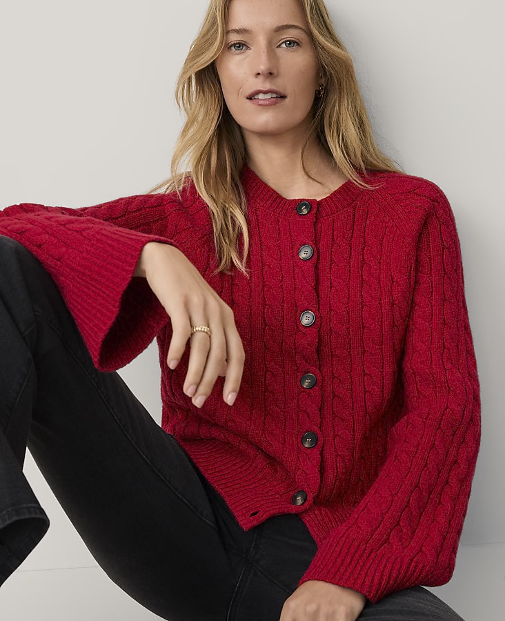 A woman wearing a red cable-knit cardigan with buttons, sitting against a neutral background.