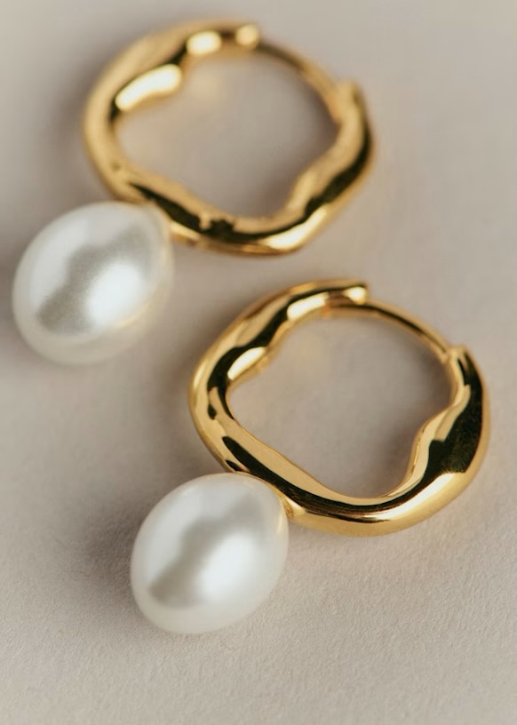 Close-up of gold hoop earrings featuring a white pearl drop.