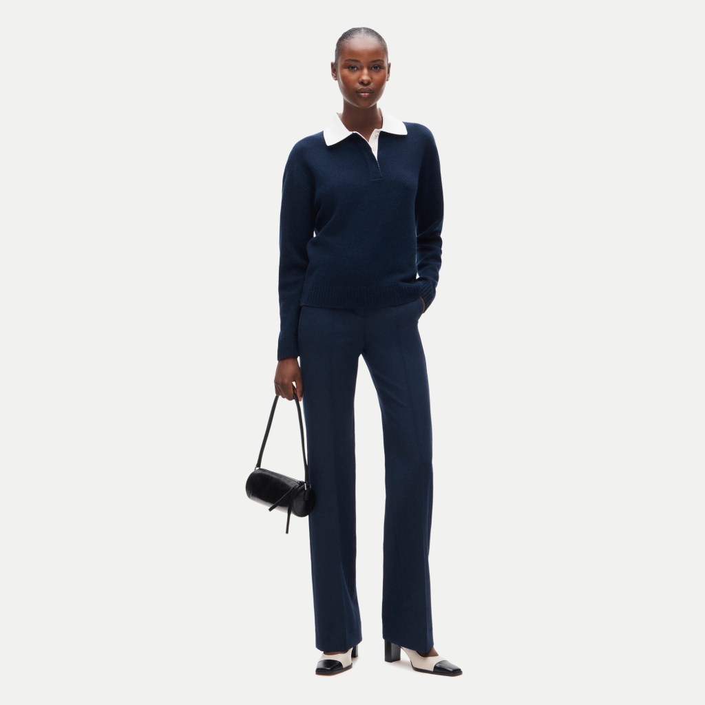 Model wearing a navy blue sweater with a white collar and matching navy trousers, holding a small black handbag.