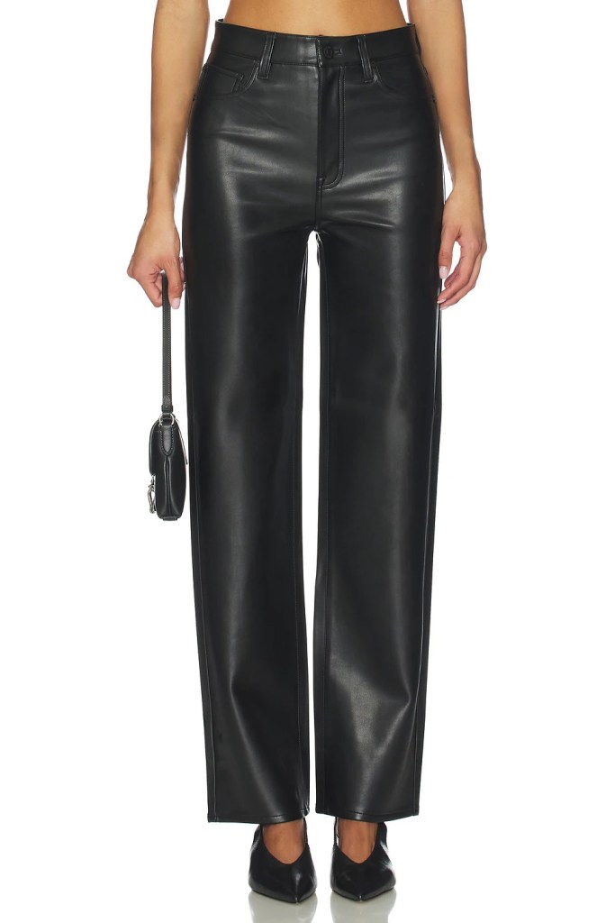 A model wearing high-waisted black faux leather pants paired with pointed toe black heels and holding a small black handbag.