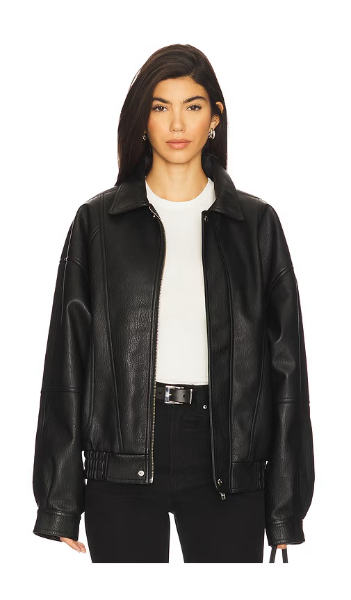 A woman wearing a black leather jacket over a white shirt, standing against a white background.