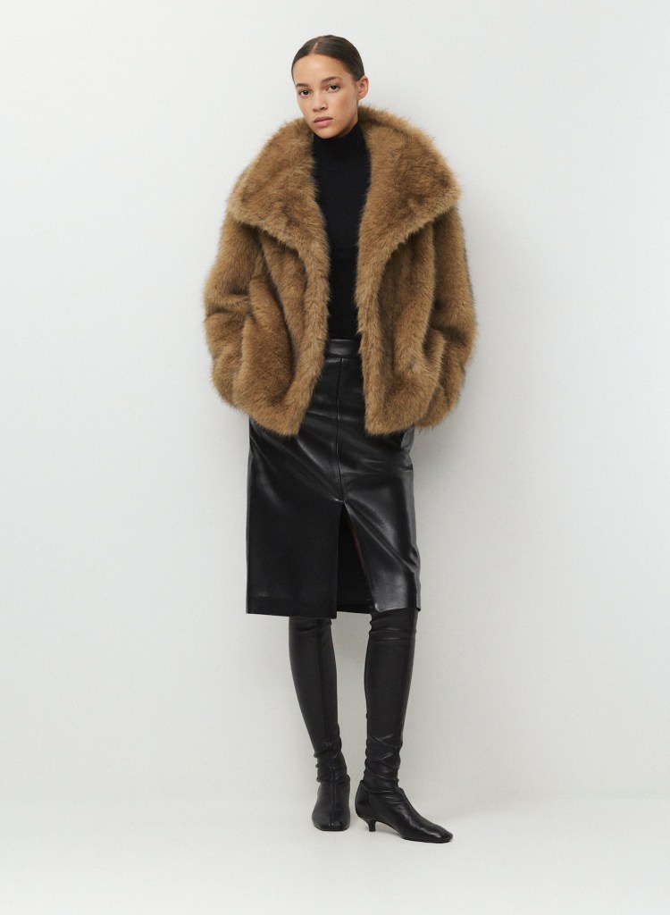 Model wearing a brown fur coat over a black turtleneck, paired with a black leather skirt and thigh-high black boots, posing against a neutral background.