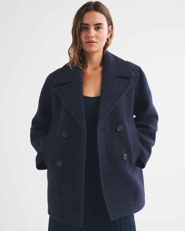 A woman wearing a dark navy double-breasted coat with large lapels, posing against a plain background.