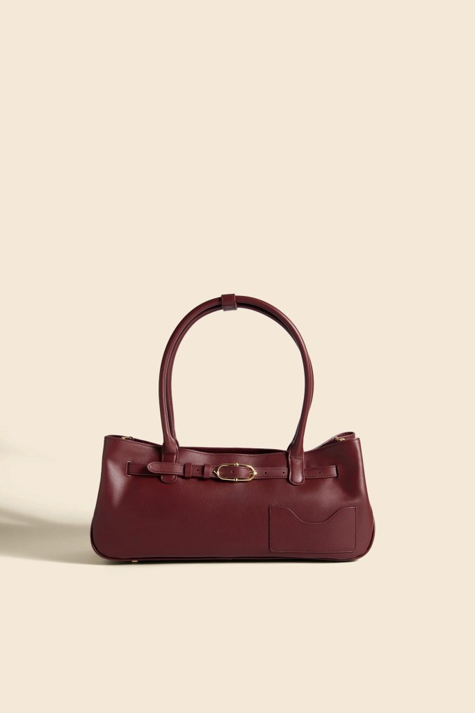 A stylish burgundy leather handbag with a long strap and a buckle detail, displayed against a soft neutral background.