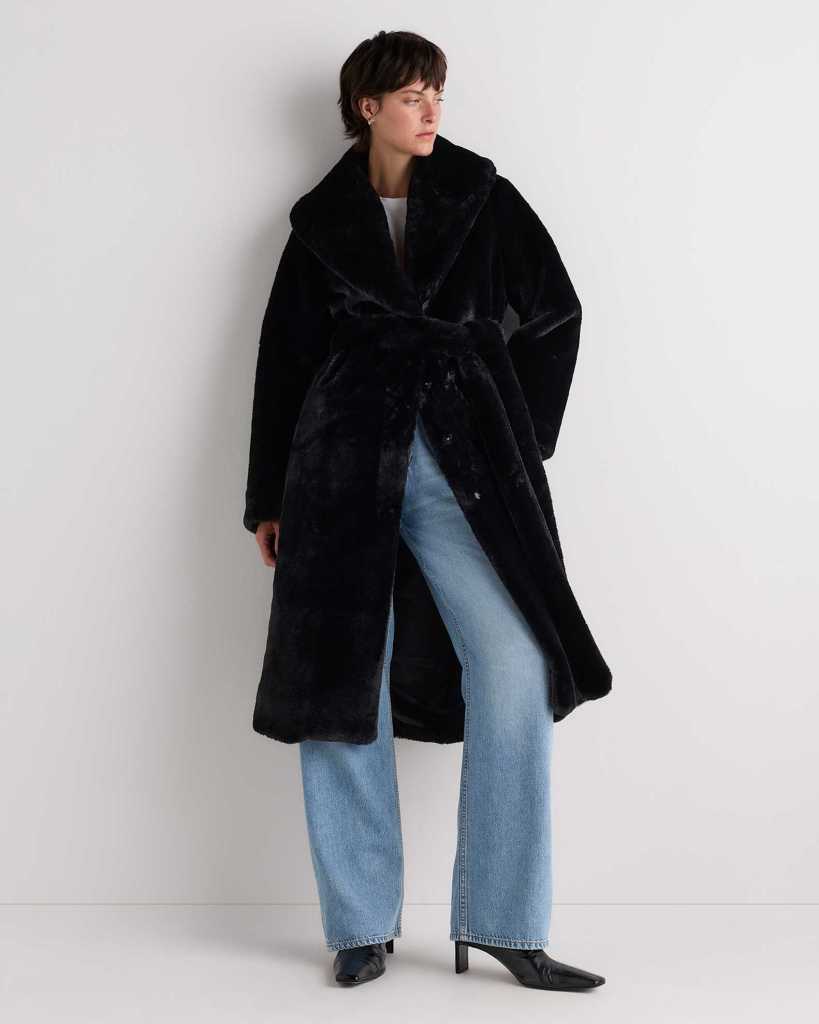 Model wearing a black faux fur coat with a wide collar, paired with light blue wide-leg jeans and black heels, posing against a plain white background.