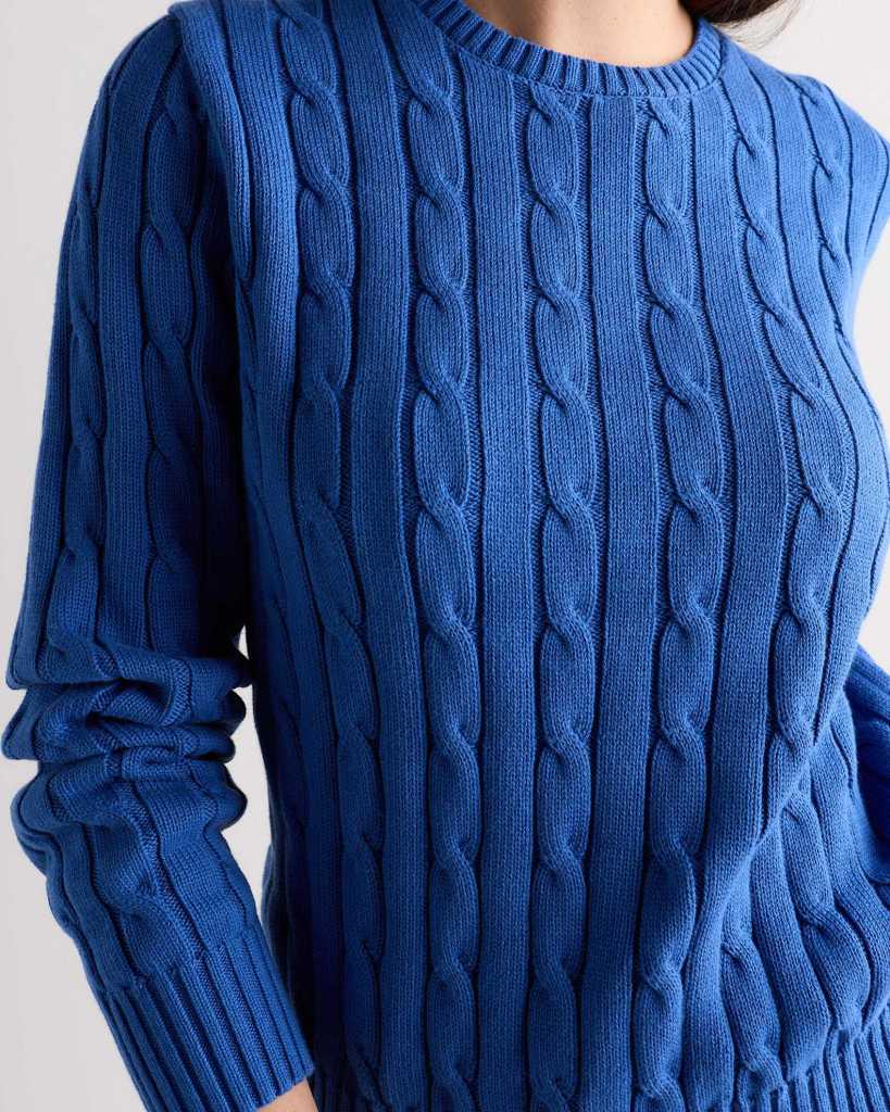 Close-up of a person wearing a ribbed blue sweater with a cable knit pattern.
